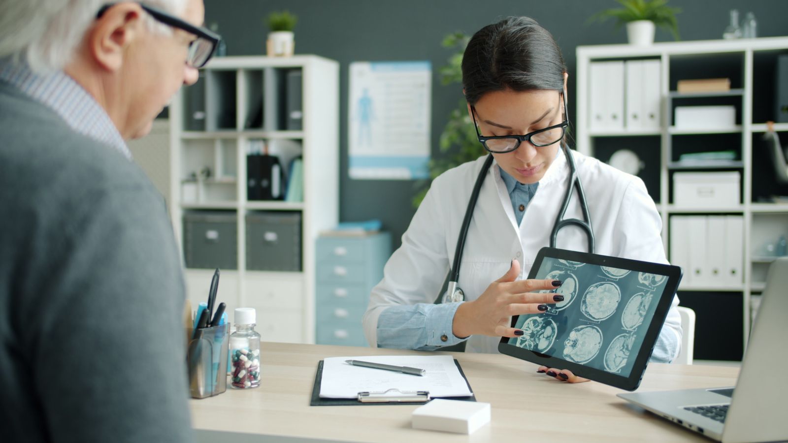Neurológ pre dospelých vysvetľuje pacientovi snímky mozgu v neurologickej ambulancii